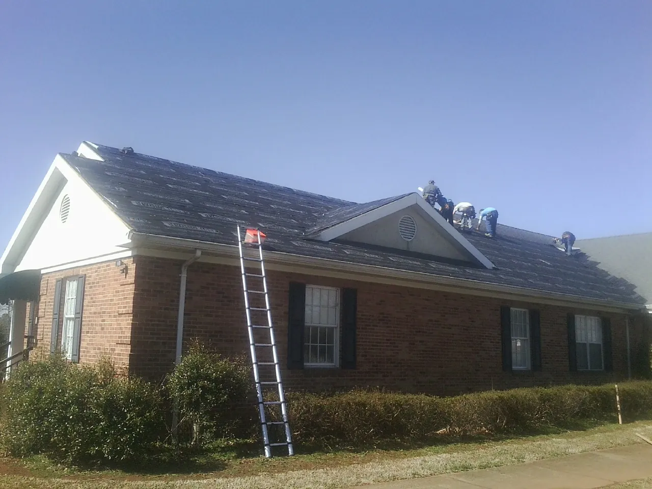 Crew tearing shingles off a brick ranch roof with a ladder set — Emergency Roof Repair work by our crew in Lodi