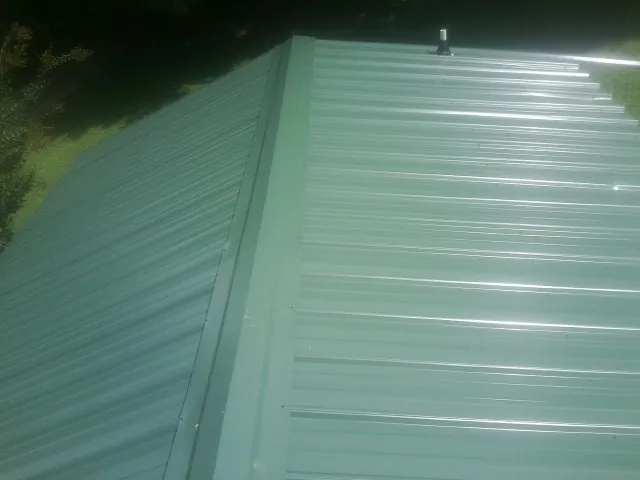 New green metal panels meeting at the ridge of a roof — Flat Roof Repair work by our crew in Lodi
